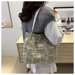 Detail of green and white woven tote bag featuring white leather straps and silver buckles
