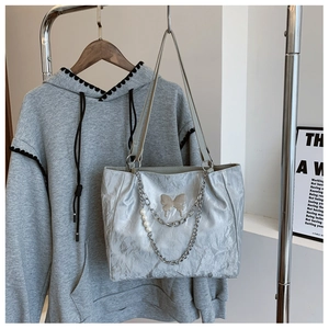 Detail of silver tote bag with metallic crinkle texture, butterfly charm and pearl chain