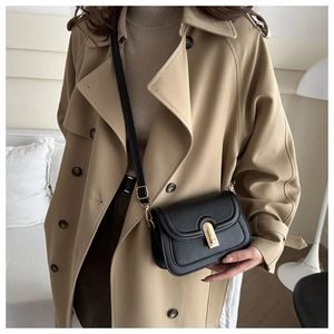 Detail of black matte leather shoulder bag with a gold horseshoe buckle on a trench coat