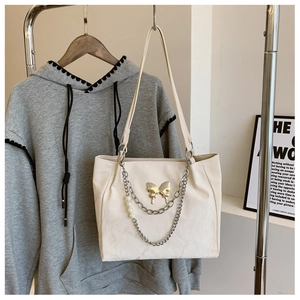 Detail of creamy white tote bag featuring golden butterfly clasp and pearl chain decor