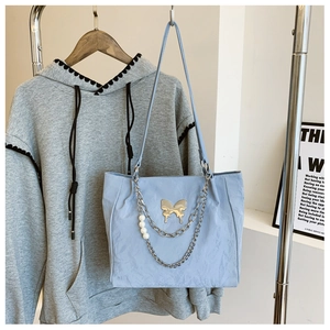Detail of light blue tote bag featuring golden butterfly, silver chain and pearl accents