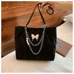 Detail of black pleated tote bag featuring white butterfly logo and pearl metal chains