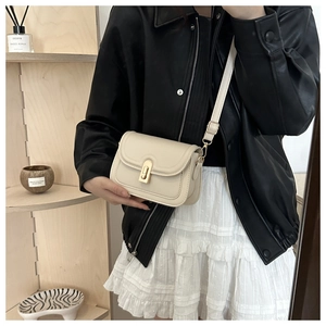 Detail of a creamy white leather crossbody bag with a golden twist lock on a stylish model