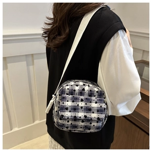 Detail of plaid crossbody bag with heart pattern and white woven strap worn by a model