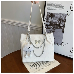 Detail of cream tote bag featuring silver butterfly charm, metal chains and cloud plushy