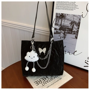 Detail of black pleated tote bag featuring metal chains, butterfly decor and cloud charm