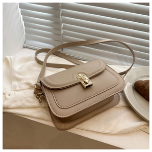 Close-up of minimalist beige crossbody bag with gold metallic twist lock on knit fabric