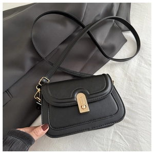 Close-up of retro black crossbody bag with gold metallic lock on white textured fabric