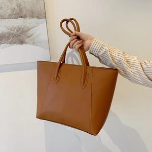Brown leather tote bag with long handles shown in a lifestyle shoulder carry view