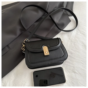 Detail of black faux leather crossbody bag with golden clasp and adjustable shoulder strap