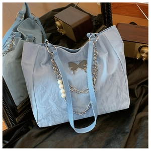 Detail of light blue tote bag with crinkled texture, silver butterfly and pearl chain