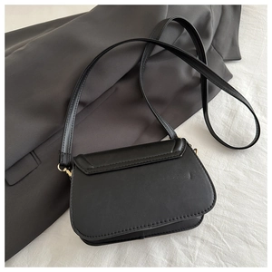 Detailed view of black PU leather crossbody bag with golden hardware on white fabric