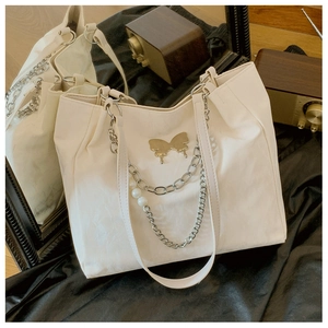 Detail of cream tote bag featuring golden butterfly hardware and pearl chain decoration