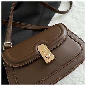 Detail of brown leather handbag with gold U-shaped twist lock and fine stitching texture