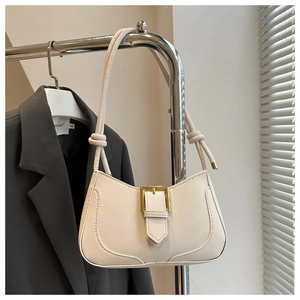 Détails rapprochés du sac crème avec boucle dorée et bandoulière à nœuds élégants