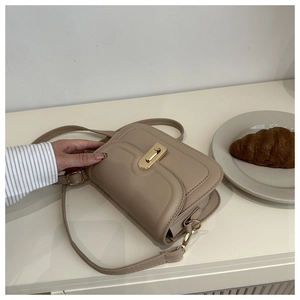 Detail of beige faux leather crossbody bag featuring a golden rectangular twist lock closure