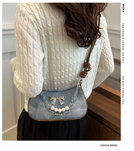 Détail du sac bandoulière en denim avec nœud argenté et chaîne de perles en demi-lune