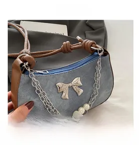 Détail d'un sac à bandoulière en denim bleu avec nœud métallique et chaîne en perles