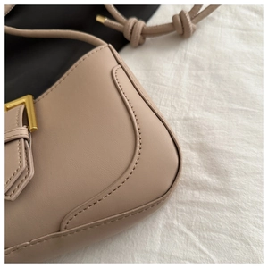 Détail d'un sac à bandoulière en cuir beige avec boucle dorée et texture de couture