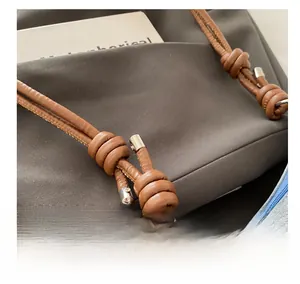 Detail of knotted brown leather shoulder strap with silver hardware on contrast bag