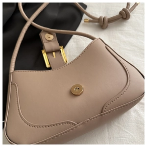 Gros plan sur le sac sous le bras en cuir beige avec boucle dorée et bandoulière ronde