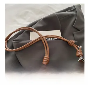 Détail d'un sac en denim bleu avec bandoulière en cuir tressé marron et chaîne argentée