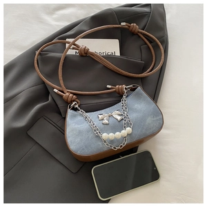 Détail du sac hobo en denim bleu avec bandoulière marron, nœud métallique et perles