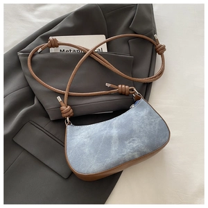 Detail of light blue denim shoulder bag with brown leather straps and bow knots