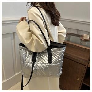 Side view of a silver quilted tote bag with long black straps on a female model