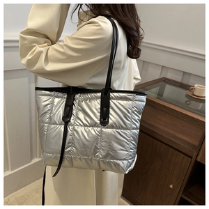 Detail of silver quilted tote bag with metallic texture and black leather shoulder straps