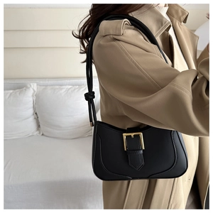 Détail d'un sac sous le bras en cuir noir avec boucle dorée sur un trench-coat beige