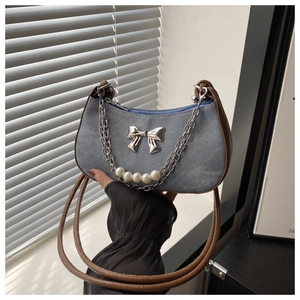 Détail du sac croissant en denim avec nœud argenté et chaîne de perles décorative