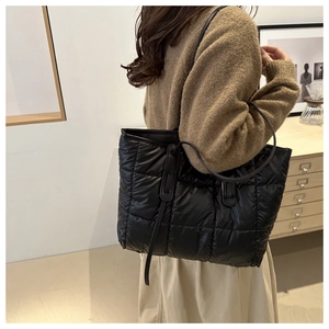 Close-up of large black quilted puffer tote bag with glossy finish on a shoulder