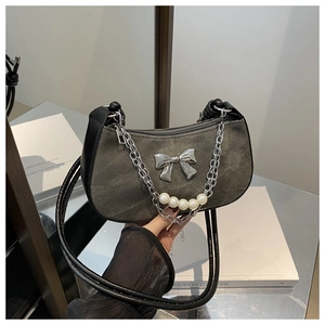 Detail of grey denim shoulder bag with silver bow and pearl chain on a glass surface