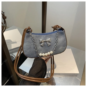 Close-up of blue denim dumpling bag featuring a silver metal bow and pearl chain detail