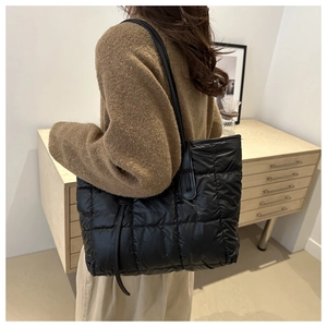 Detail of a large black quilted tote bag with soft padded texture and dual shoulder straps