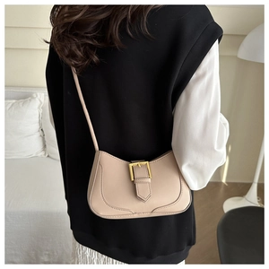 Gros plan du sac hobo beige avec boucle dorée sur un modèle en intérieur