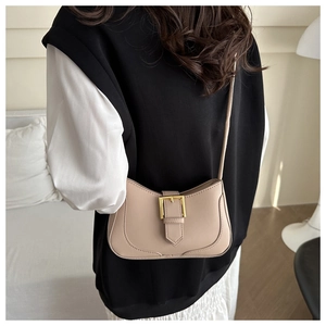 Détail d'un sac à bandoulière en cuir beige avec boucle dorée porté par un mannequin