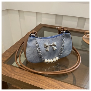 Close-up of denim shoulder bag with silver bow detail and pearl accented metal chain
