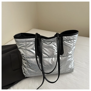 Macro shot of silver quilted tote bag featuring metallic finish and black leather straps