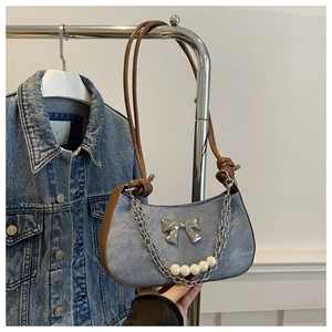 Détail du sac sous le bras en denim avec nœud argenté et éléments de chaîne de perles