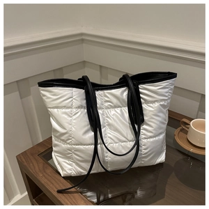 White quilted puffer tote bag with black leather straps on a wooden table in home setting