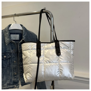 Detail of white quilted puffer tote bag featuring black handle straps and spacious design