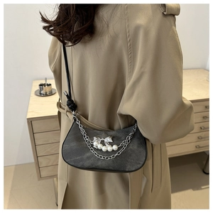 Detail of grey denim crescent bag with metal chains and pearl bow charm on model