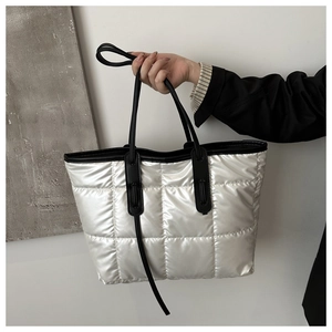 Detail of white quilted tote bag with metallic finish and black leather handles