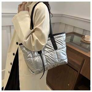 Close-up of metallic silver quilted puffer tote bag with black shoulder straps and modern texture