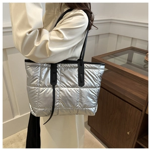 Detail of silver quilted puffer tote bag featuring black contrast straps and metallic finish