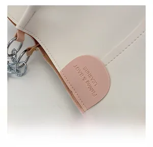Macro detail of creamy white PU leather tote with embossed logo and silver chain strap