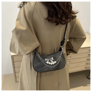 Detail of dark denim crescent bag with metal chain, silver bow and pearl accents