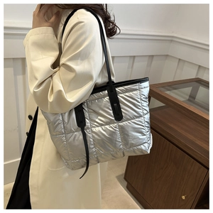 Close-up of shiny silver quilted tote bag with black straps and square stitching